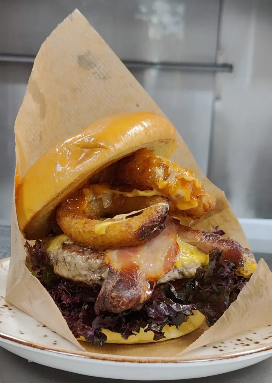 Burger with onion rings and melted cheese served in paper